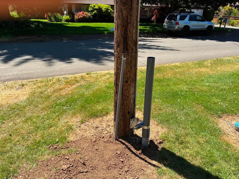 Wooden utility pole with metal reinforcement bracket on grassy lawn near driveway with parked vehicles
