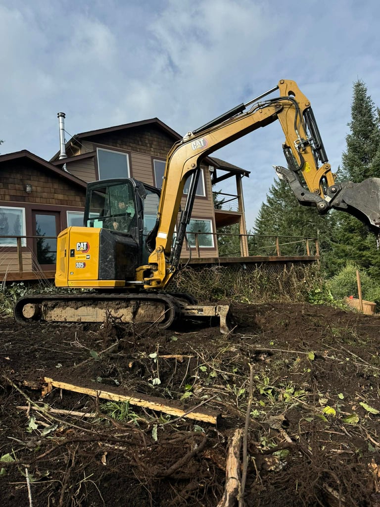 Yellow CAT mini excavator working on clearing dirt and debris near a residential house with pine trees